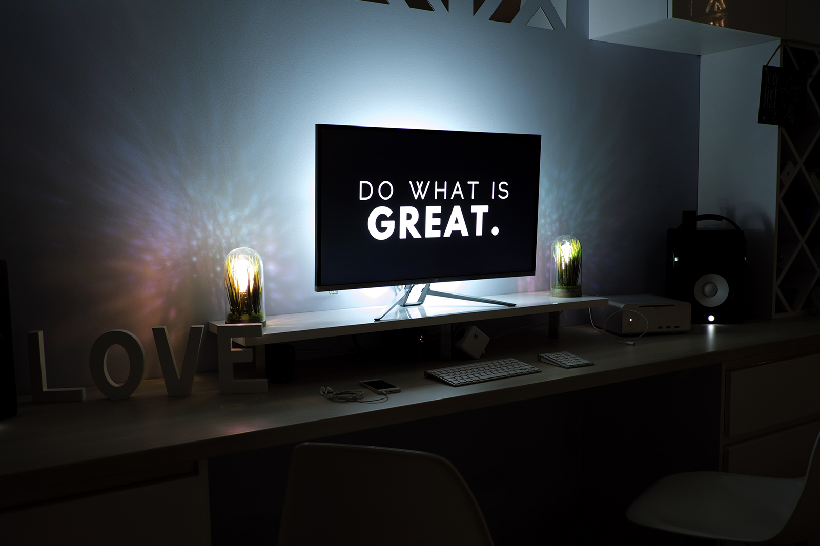 Computer screen on a table with a sign that reads "DO WHAT IS GREAT".
