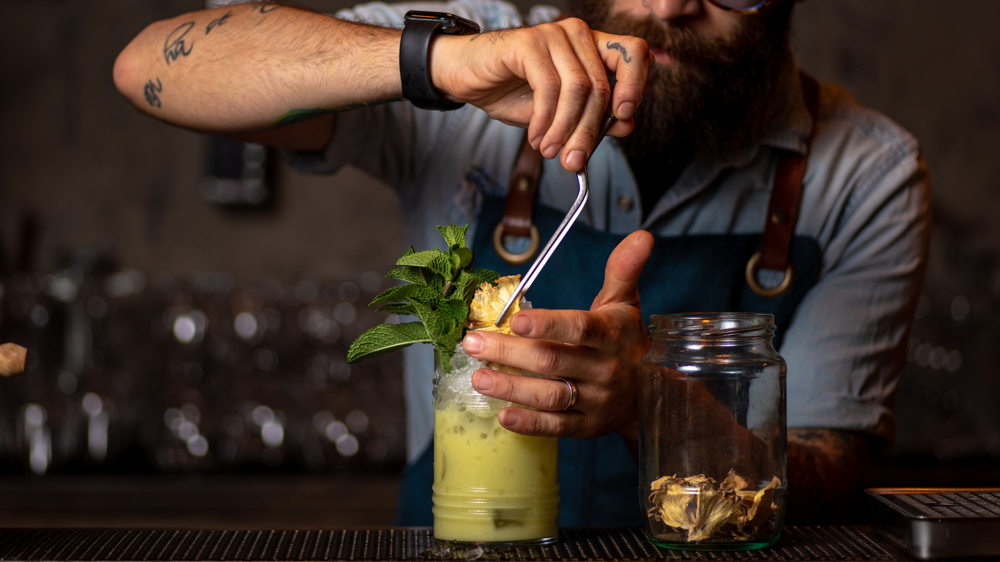 Bartender putting a metal straw on a yellow mushroom cocktail.