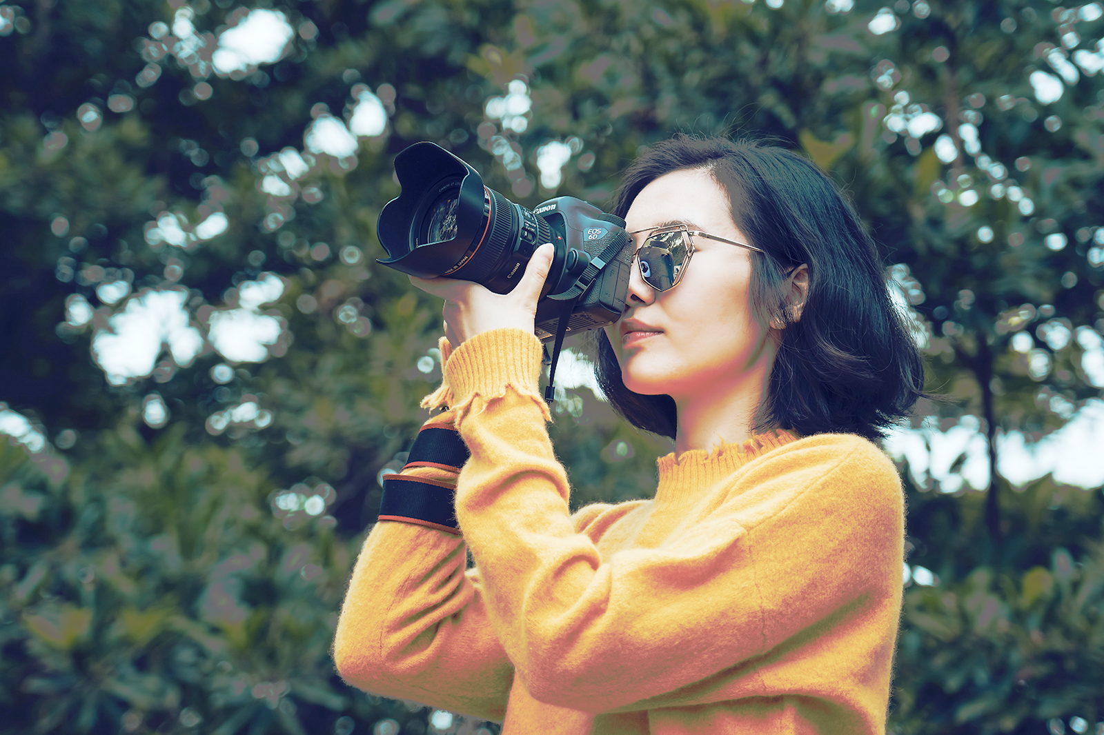 Woman wearing sunglasses taking a photo with a professional camera outdoors.